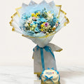 Bouquet of flowers wrapped in light blue paper with a small cake on a white background