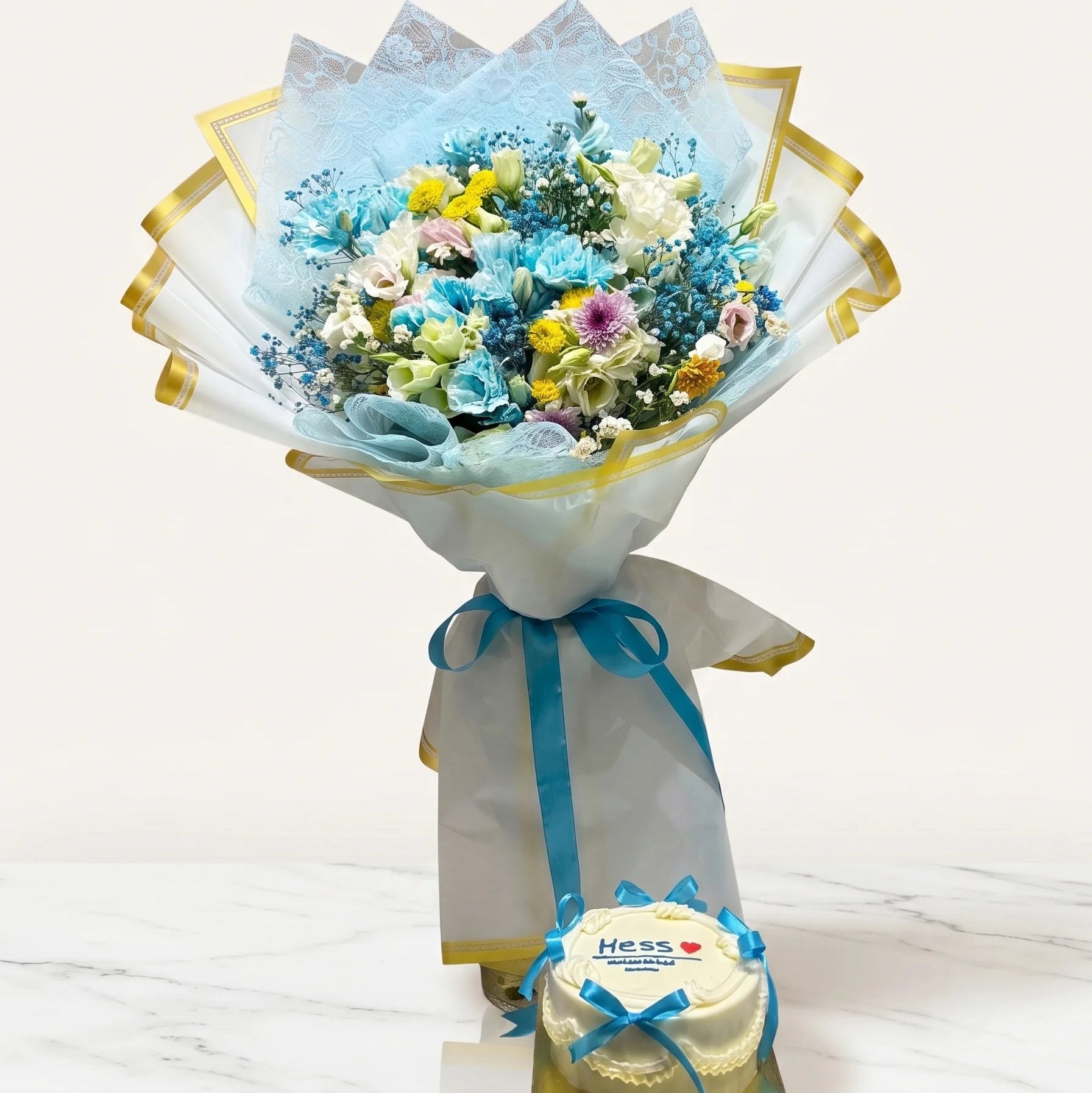 Bouquet of flowers wrapped in light blue paper with a small cake on a white background