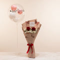 Bouquet of red roses with a decorative bow on a marble surface, with balloons and gift boxes in the background.