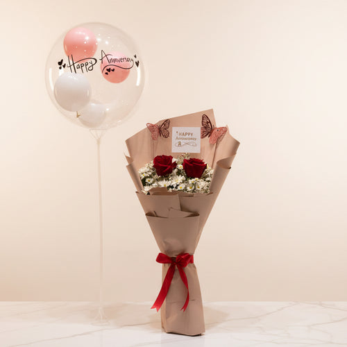 Bouquet of red roses with a decorative bow on a marble surface, with balloons and gift boxes in the background.