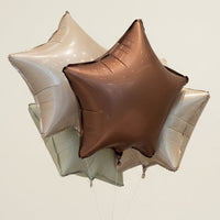 Star-shaped balloons and a bouquet of flowers with a red ribbon on a marble surface, with a store interior in the background.