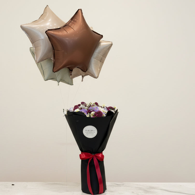 Star-shaped balloons and a bouquet of flowers with a red ribbon on a marble surface, with a store interior in the background.