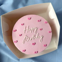 Pink birthday cake with 'Happy Birthday' text on a blue fabric background