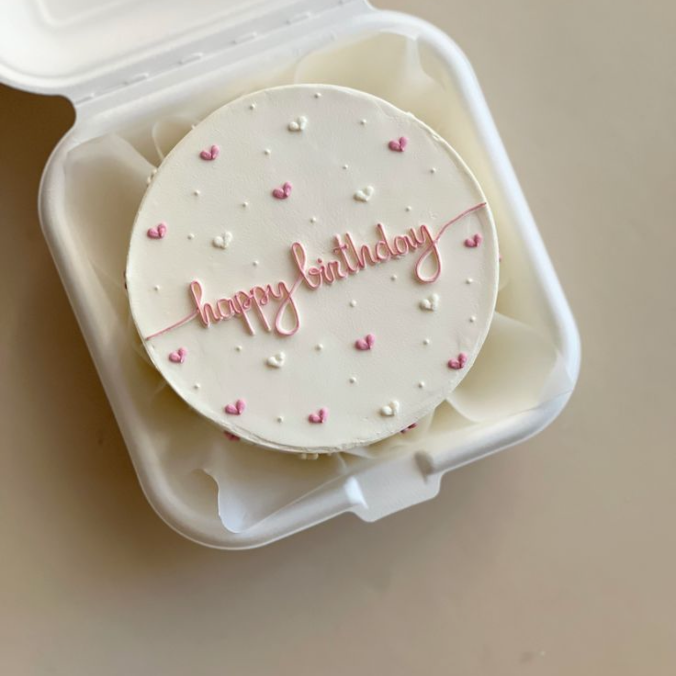 Small round container with a lid, featuring 'happy birthday' text and heart designs, on a beige background.