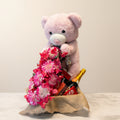 Pink teddy bear with a bouquet of flowers in front of a colorful fabric background