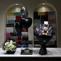 A black memorial balloon bouquet with a heart-shaped balloon and a black flower arrangement with a teddy bear bouquet, displayed on a marble counter in front of a gift shop background.
