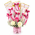 A decorative bouquet arrangement made from wrapped gift boxes tied with pink ribbons and bows, accented with white and pink roses, baby's breath, and small green stems, displayed on a marble-like surface with a blurred shop background.