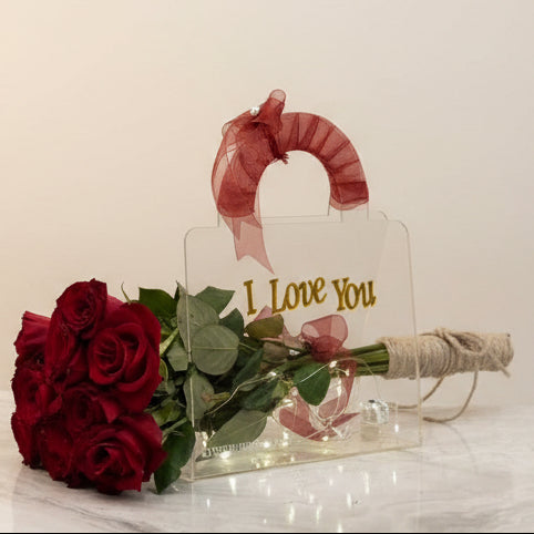 Red rose and 'I Love You' card on a marble surface with fabric rolls in the background