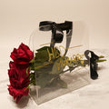 Clear holder with red roses and 'His & Hers' jewelry on a marble surface with fabric background