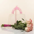 Clear acrylic stand with pink floral arch and roses on a white surface.